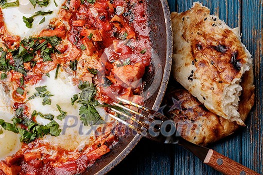 Fried eggs in a frying pan with tomatoes, sausage and greens.