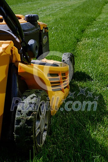 Yellow lawn mower on the green grass. Caring for a garden. Shallow depth of field.