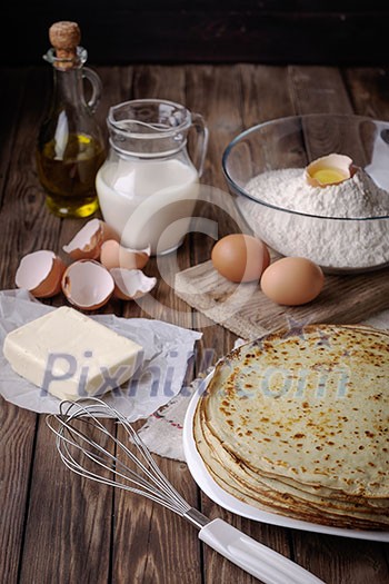 Stack of crepes and ingredients for cooking on a wooden table.
