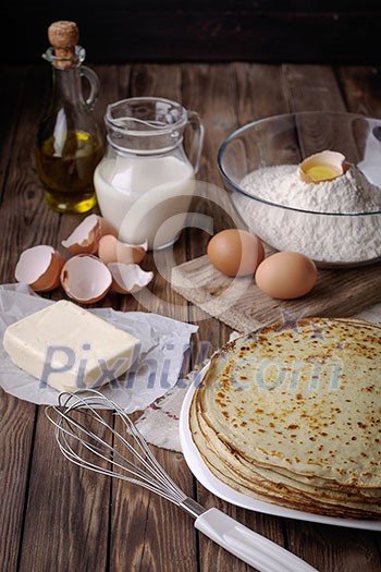 Stack of crepes and ingredients for cooking on a wooden table. Stack of crepes and ingredients for cooking on a wooden table.