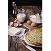 Stack of crepes and ingredients for cooking on a wooden table.