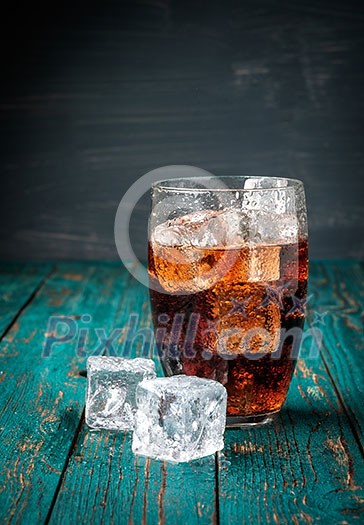 Glass of cola with ice on a wooden table. Copyspace.