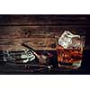 Glass of whiskey with ice and pipe on a wooden background. Vintage toned.