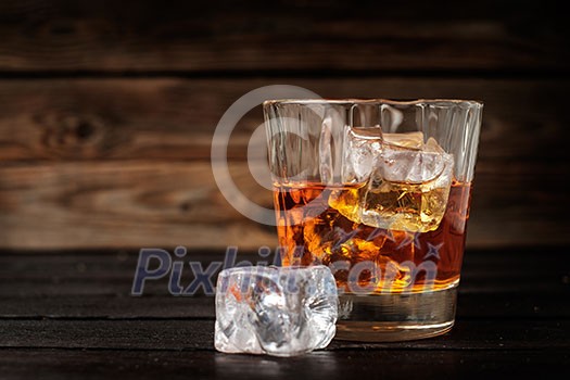 Glass of whiskey with ice on a wooden background. Copyspace on the left. Glass of whiskey with ice on a wooden background. Copyspace on the left.