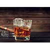 Glass of whiskey with ice and cigar on a wooden background. Vitage toned.