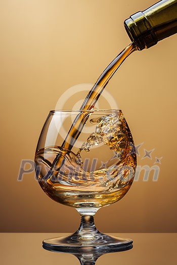 Cognac pouring from bottle into glass with splash on brown background Cognac pouring from bottle into glass with splash on brown background