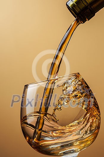 Cognac pouring from bottle into glass with splash on brown background Cognac pouring from bottle into glass with splash on brown background