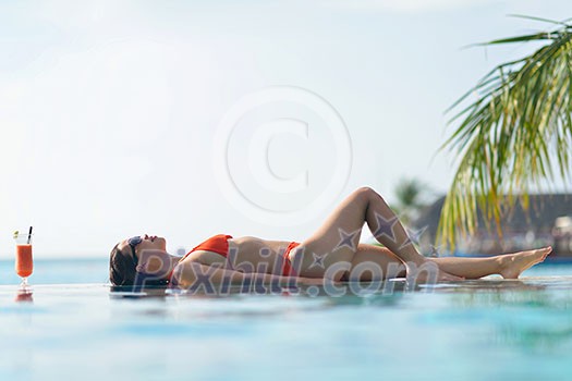 Beautiful young woman in bikini lying on a deckchair with a drink by the sea Beautiful young woman in bikini lying on a deckchair with a drink by the sea