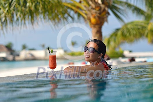 Beautiful young woman in bikini lying on a deckchair with a drink by the sea