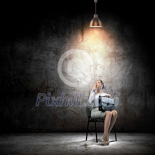 Image of young businesswoman sitting on chair under spot of light Image of young businesswoman sitting on chair under spot of light