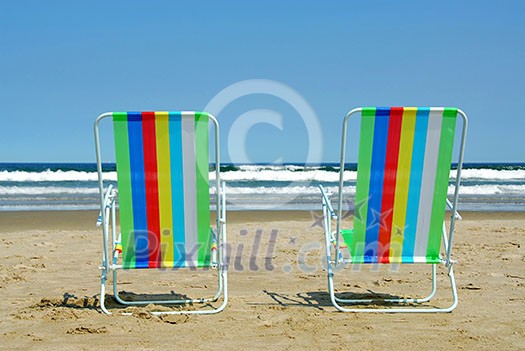 Two colorful beach chairs on the ocean shore Two colorful beach chairs on the ocean shore