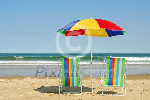Beach chairs and umbrella on the ocean shore with surf in the background, horisontal