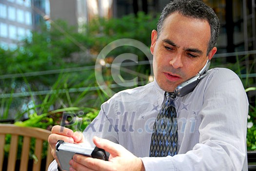Portrait of a busy businessman in the city using pda and cell phone