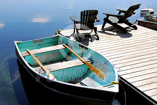 Two wooden adirondack chairs on a boat dock on a beautiful still lake with sky reflection