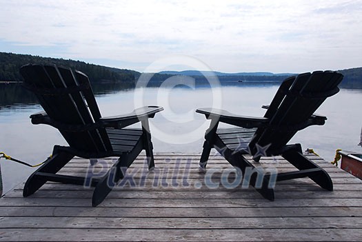 Two wooden adirondack chairs on a boat dock on a beautiful lake in the evening