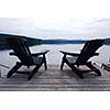 Two wooden adirondack chairs on a boat dock on a beautiful lake in the evening