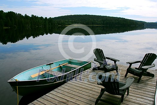 Three wooden adirondack chairs on a boat dock on a beautiful lake in the evening