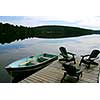 Three wooden adirondack chairs on a boat dock on a beautiful lake in the evening