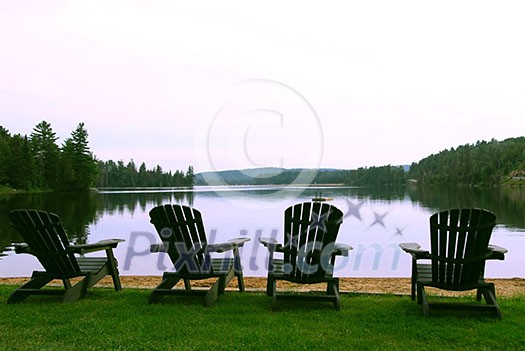 Four wooden adirondack chairs on a shore of a beautiful lake at dusk