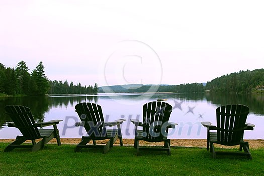 Four wooden adirondack chairs on a shore of a beautiful lake at dusk Four wooden adirondack chairs on a shore of a beautiful lake at dusk