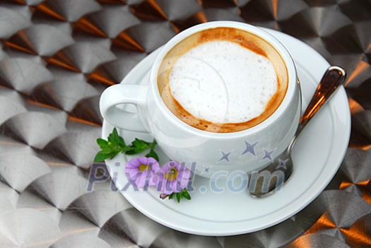 Cup of coffee with flowers on saucer on a table with metallic surface Cup of coffee with flowers on saucer on a table with metallic surface