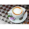 Cup of coffee with flowers on saucer on a table with metallic surface