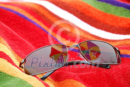 Sunglasses on beach towel relfecting beach umbrella above them