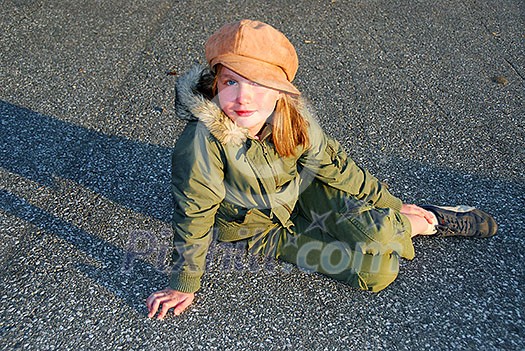 Young girl in a hat sitting on pavement, evening sun