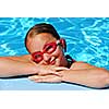 Portrait of a young girl in red goggles resting at the pool edge