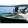 Paddle boat and two adirondack wooden chairs on dock facing a blue lake 
