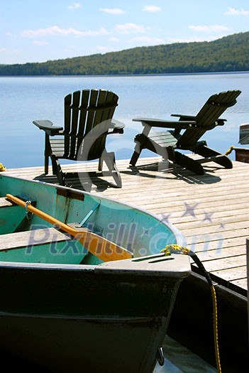 Paddle boat and two adirondack wooden chairs on dock facing a blue lake Paddle boat and two adirondack wooden chairs on dock facing a blue lake