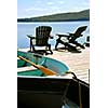 Paddle boat and two adirondack wooden chairs on dock facing a blue lake