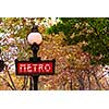 Red metro sign in Paris France on background of fall trees