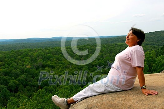 Mature woman sitting on cliff edge enjoying scenery Mature woman sitting on cliff edge enjoying scenery