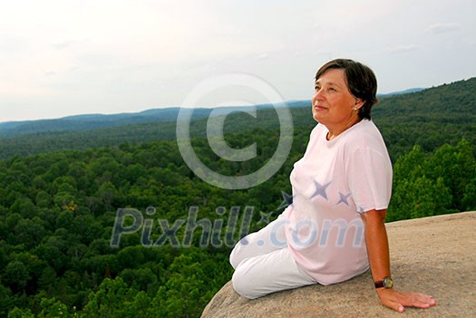 Mature woman sitting on cliff edge enjoying scenery Mature woman sitting on cliff edge enjoying scenery