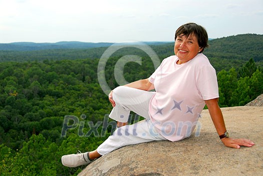 Mature woman sitting on scenic cliff edge smiling Mature woman sitting on scenic cliff edge smiling