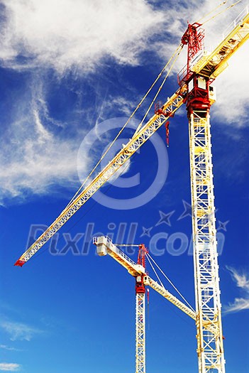 Two construction cranes on blue sky background