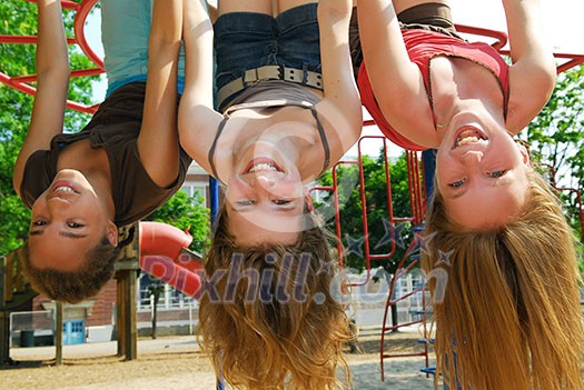 Three young girls hanging upside down in a park and laughing