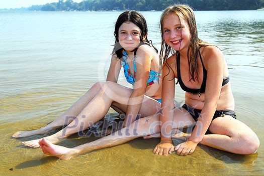 Two preteen girls sitting in shallow water on a beach Two preteen girls sitting in shallow water on a beach