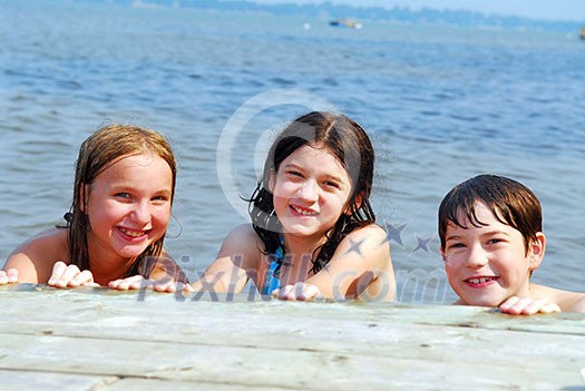 Portrait of three children holding onto wooden dock at the lake