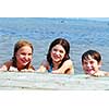Portrait of three children holding onto wooden dock at the lake