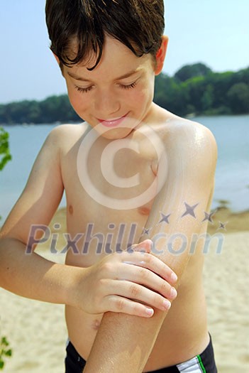 Young boy applying sunscreen to his skin on a beach