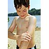 Young boy applying sunscreen to his skin on a beach
