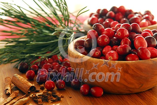 Fresh red cranberries in wooden bowls with spices and pine branches Fresh red cranberries in wooden bowls with spices and pine branches