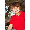 Young boy sitting on a tree branch in summer park