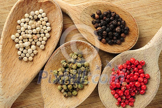 Four kinds of peppercorns in wooden cooking spoons