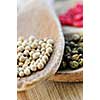 Different kinds of peppercorns in wooden cooking spoons macro