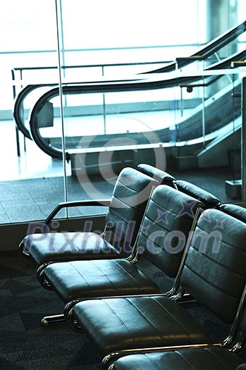 Row of chairs and escalator inside an airport Row of chairs and escalator inside an airport