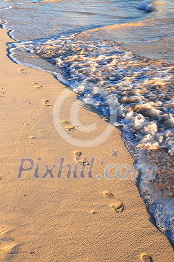 Footprints on sandy tropical beach washed away by waves