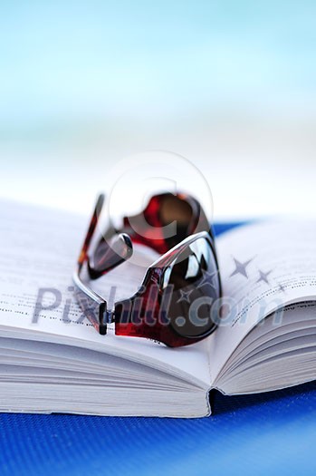 Sunglasses and open book on beach chair - summer vacation concept Sunglasses and open book on beach chair - summer vacation concept